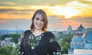 Woman standing on a roof top with sunset and city in background